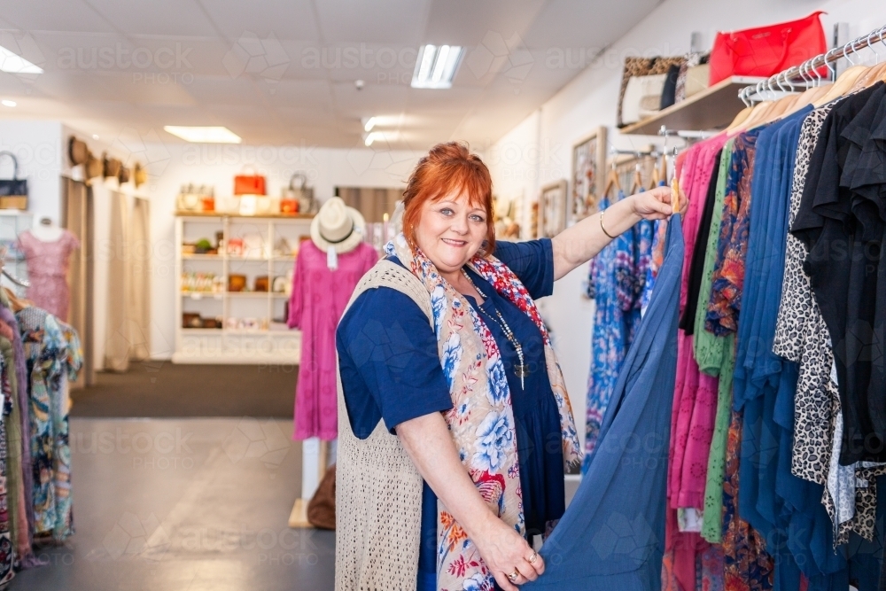 Portrait of a happy middle aged woman shopping in clothing store for a new outfit - Australian Stock Image