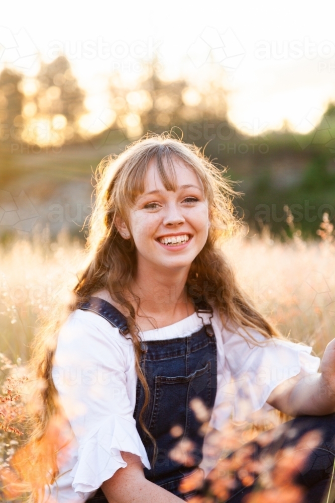 Portrait of a happy smiling young woman at sunset in fluffy grass - Australian Stock Image