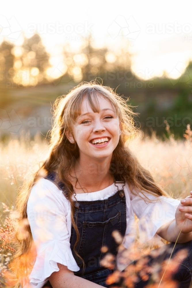 Portrait of a happy smiling young woman at sunset in fluffy grass - Australian Stock Image