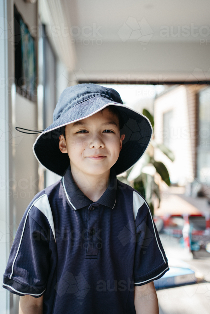 Portrait of a happy young boy in school uniform wearing a bucket hat - Australian Stock Image