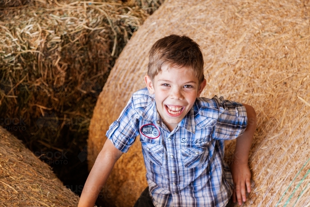 Portrait of a happy young boy on hay bales in a shed - Australian Stock Image