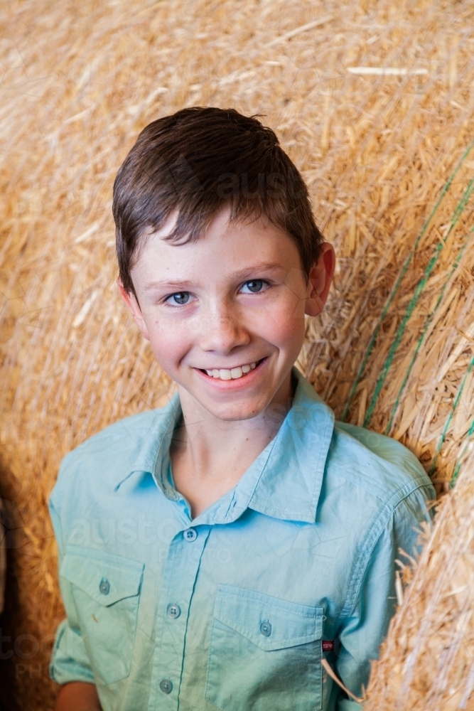 Portrait of a happy young boy on hay bales in a shed - Australian Stock Image