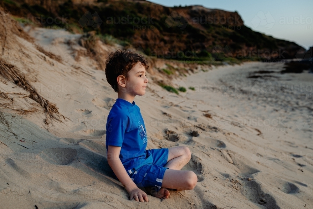 Portrait of a happy young boy relaxing on on the beach at sunset - Australian Stock Image