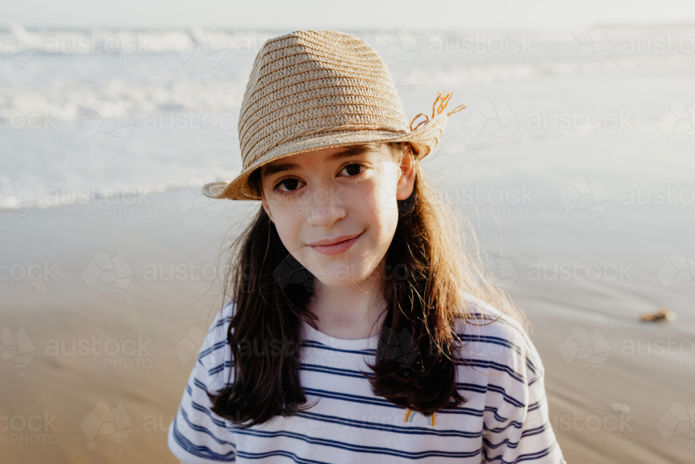 Portrait of a happy young girl wearing a sunhat at the beach in the afternoon looking at the camera - Australian Stock Image