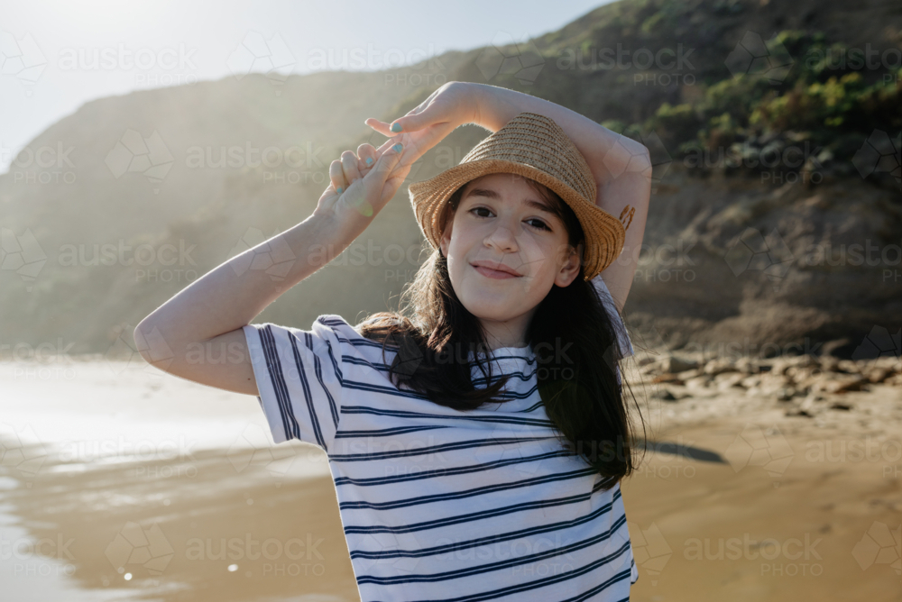 Portrait of a happy young girl wearing a sunhat looking at the camera at the beach in the afternoon - Australian Stock Image