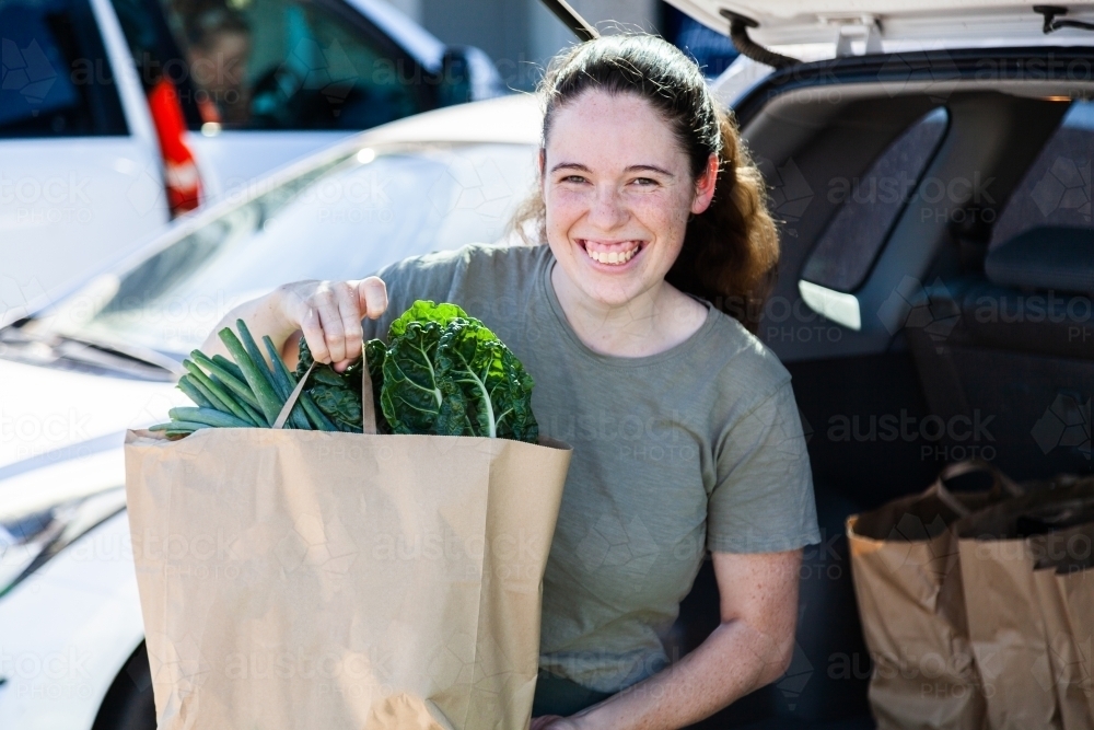 Portrait of a happy young woman loading groceries into the car boot - Australian Stock Image