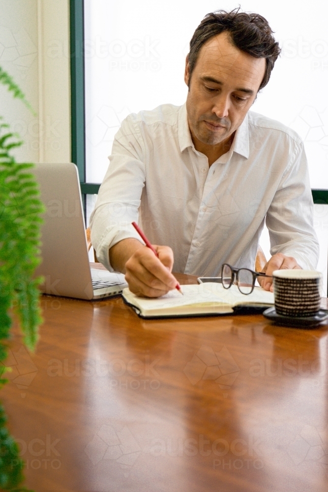 Portrait of a male office worker sitting with laptop and note book at a meeting table - Australian Stock Image
