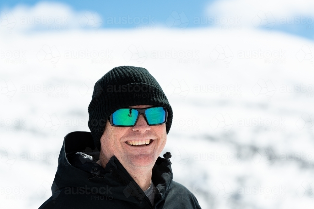 Portrait of a man looking down dressed in warm black outdoor coat and cap with blurred snow-covered - Australian Stock Image