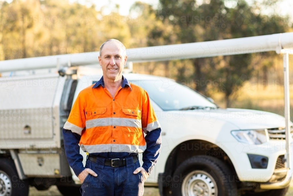 Portrait of a middle age tradie in high vis standing in front of work vehicle ute - Australian Stock Image