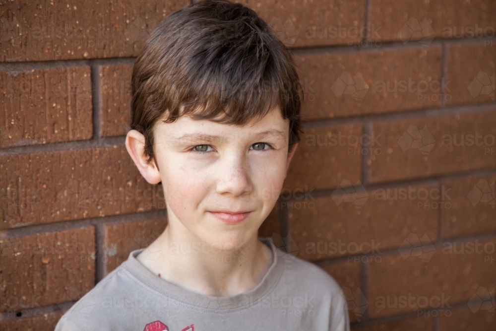 Portrait of a nine year old boy standing against brick wall - Australian Stock Image