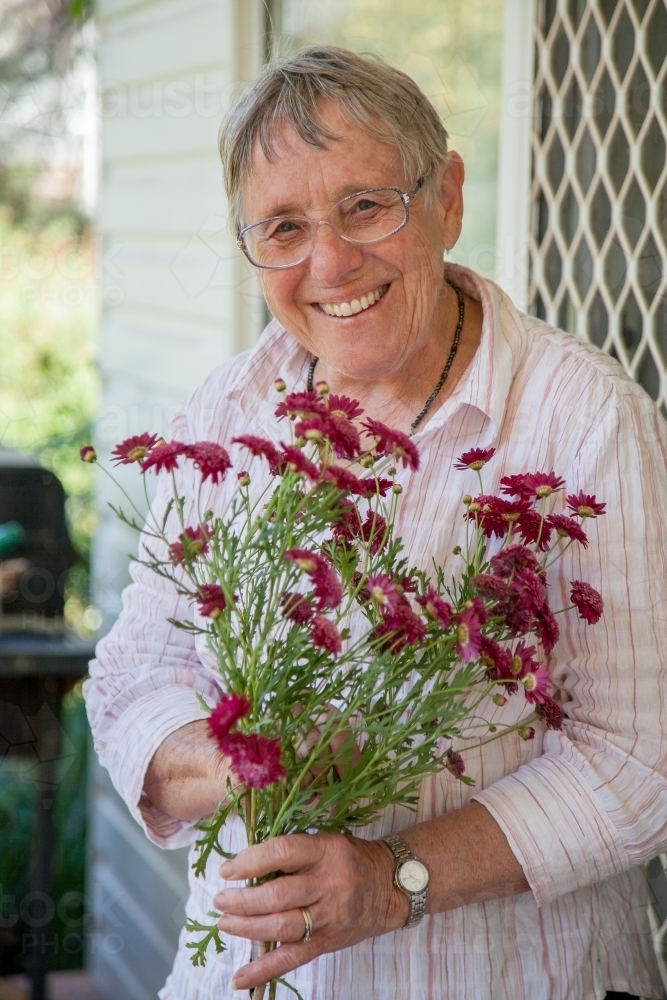 Portrait of a smiling retiree holding flowers - Australian Stock Image