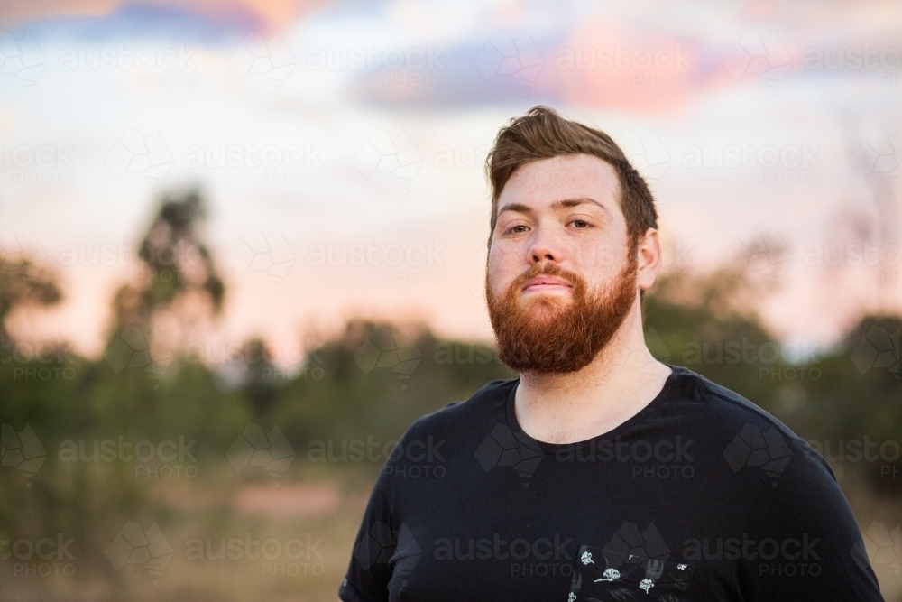 Portrait of a young aussie man with beard, outside at dusk wearing black t-shirt - Australian Stock Image