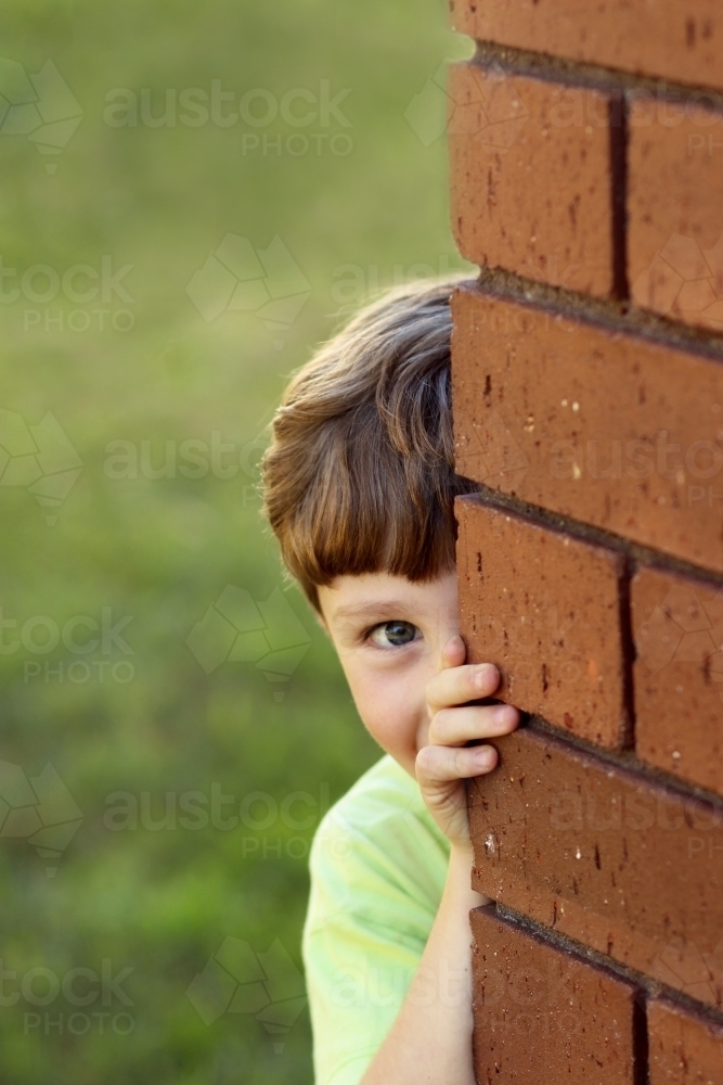 Portrait of a young boy looking around the corner of the house - Australian Stock Image