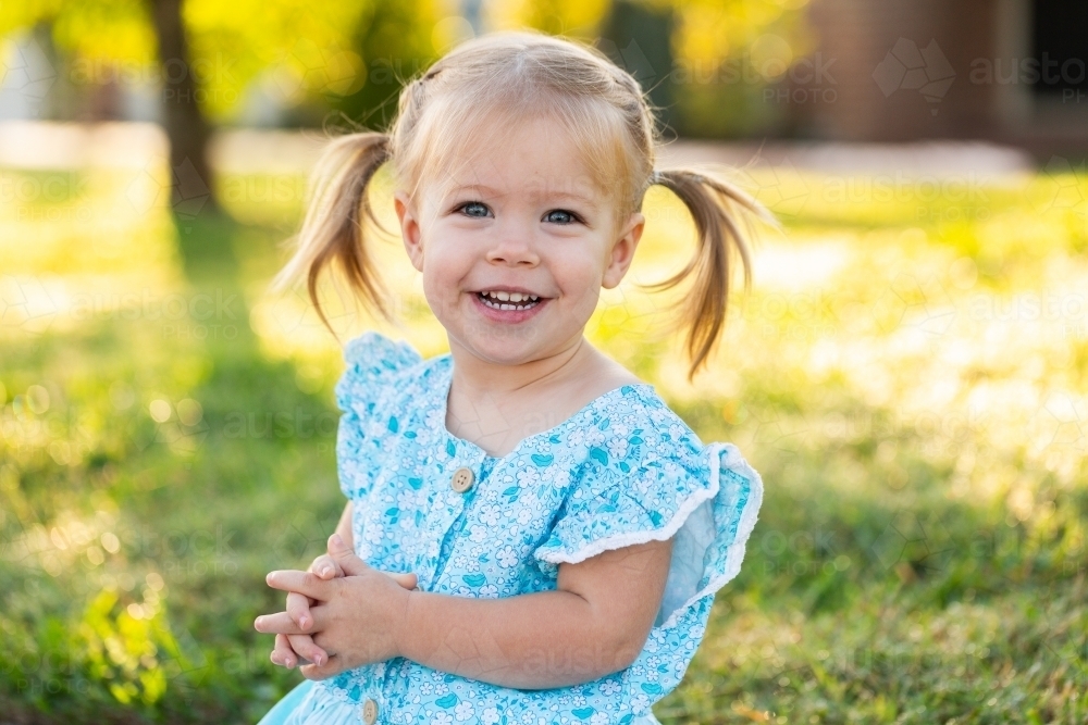 Portrait of a young girl in blue dress and pigtails smiling - Australian Stock Image