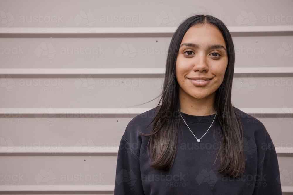 Portrait of a young, smiling,  first nations woman against wall outside - Australian Stock Image