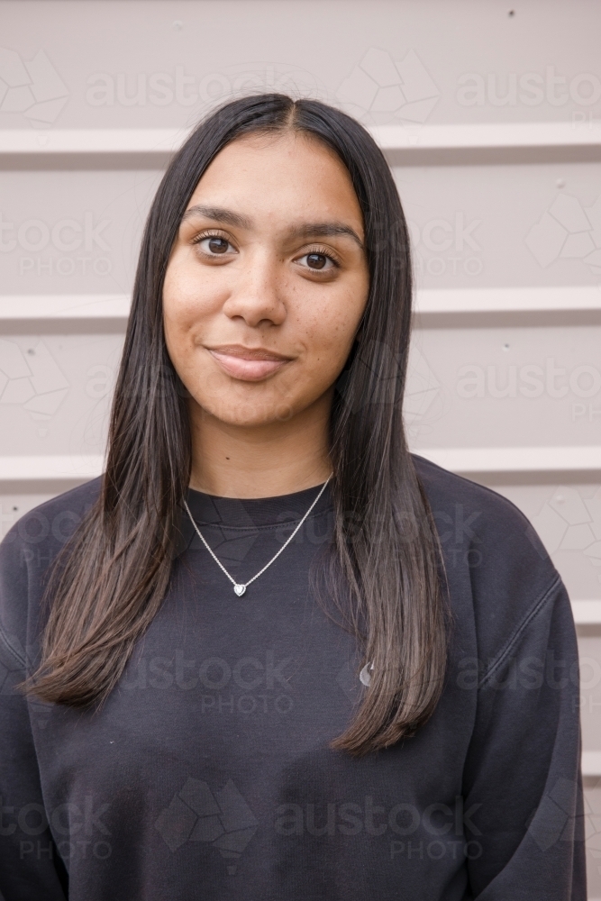 Portrait of a young, smiling, first nations woman against wall outside - Australian Stock Image