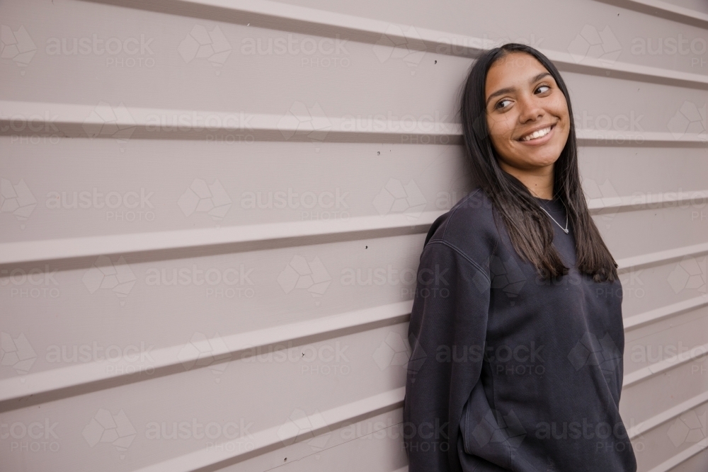 Portrait of a young, smiling,  first nations woman against wall outside - Australian Stock Image