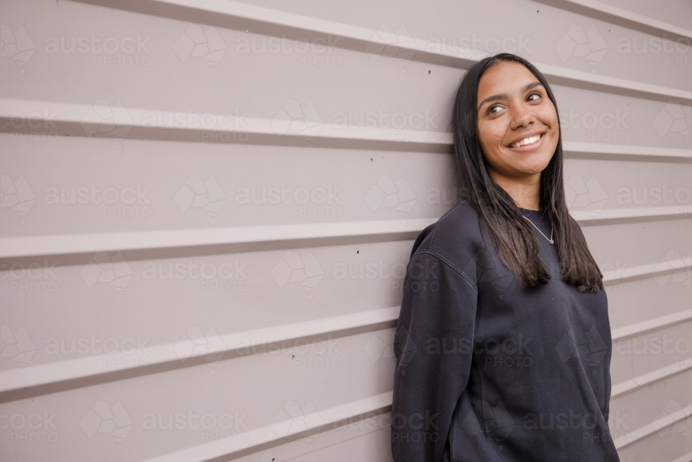 Portrait of a young, smiling,  first nations woman against wall outside - Australian Stock Image