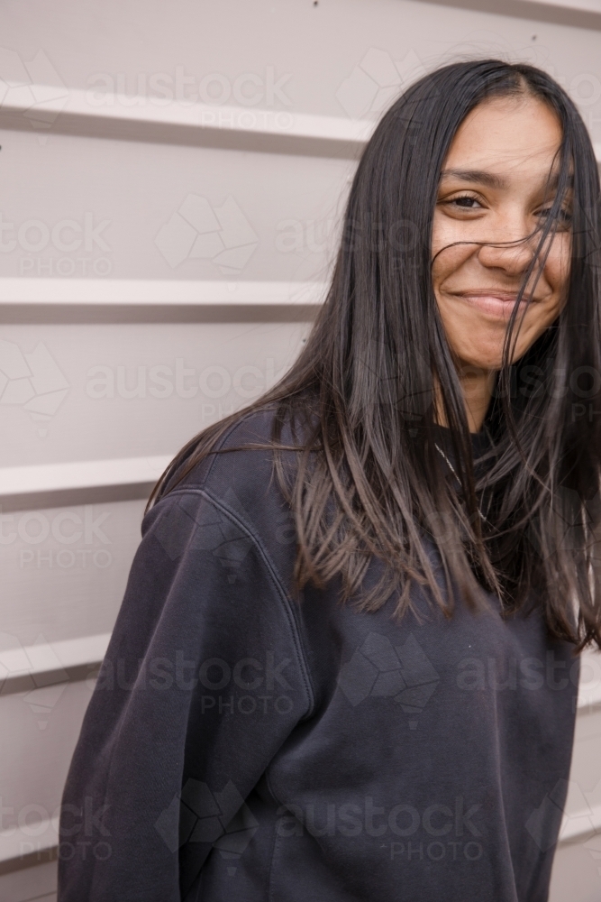 Portrait of a young, smiling, first nations woman against wall outside - Australian Stock Image