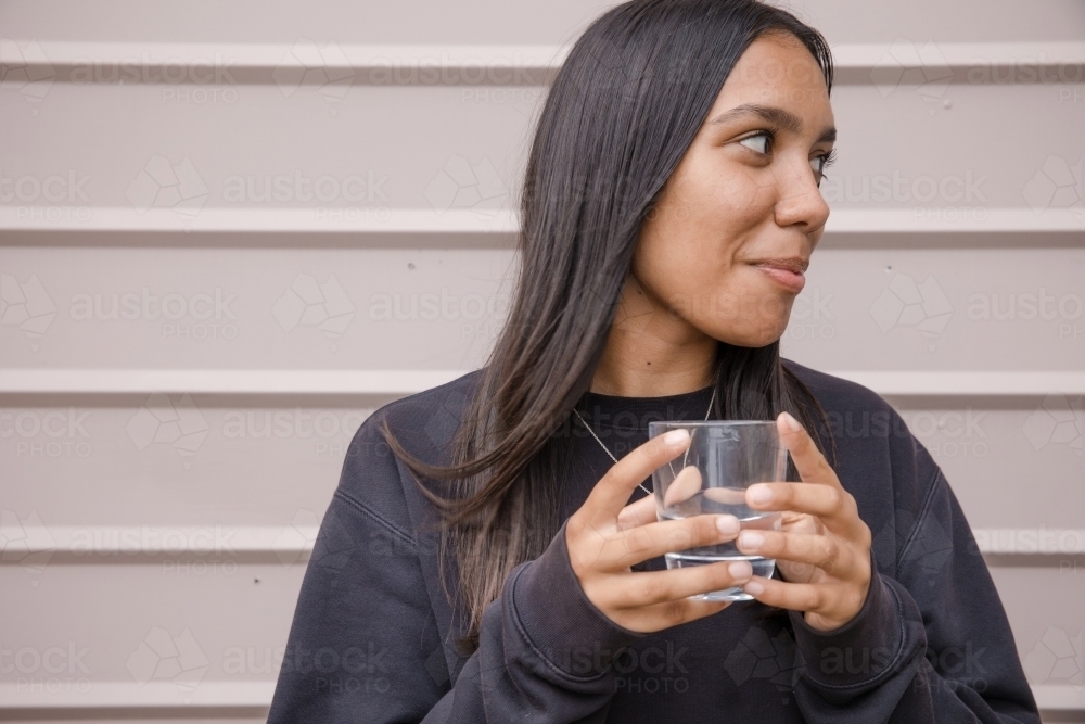 Portrait of a young, smiling, first nations woman holding a glass of water - Australian Stock Image