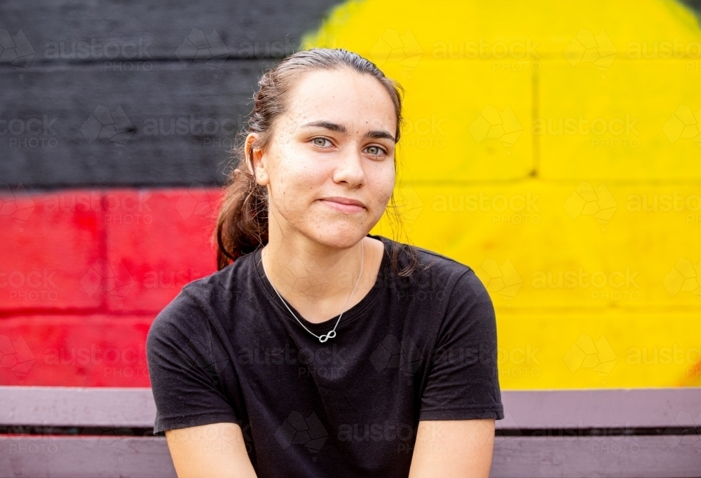 Portrait of an Aboriginal woman sitting in front of a painted wall - Australian Stock Image