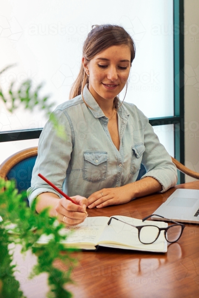 Portrait of an office worker sitting with laptop and note book at a meeting table - Australian Stock Image