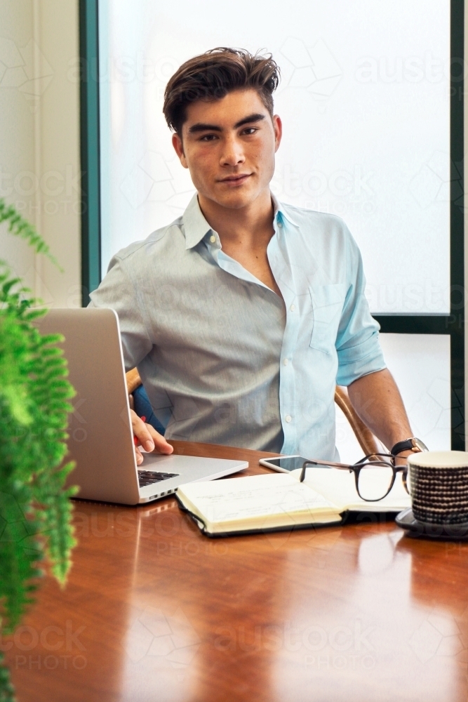 Portrait of an office worker sitting with laptop and note book at a meeting table - Australian Stock Image