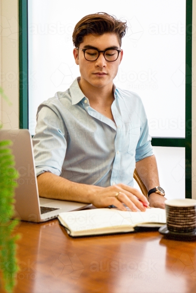 Portrait of an office worker sitting with laptop and note book at a meeting table - Australian Stock Image