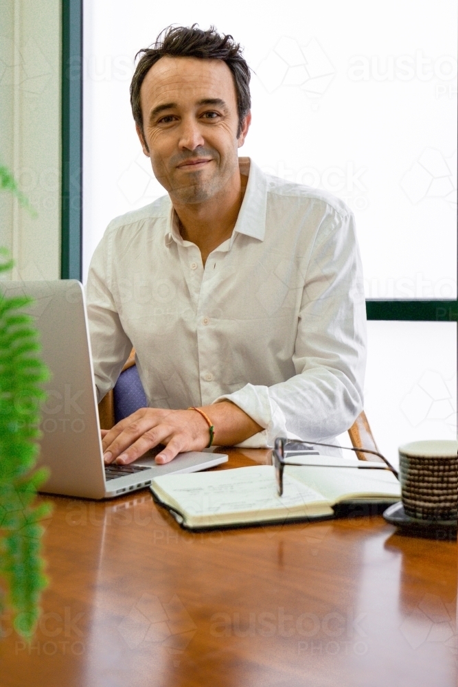 Portrait of an office worker sitting with laptop and note book at a meeting table - Australian Stock Image