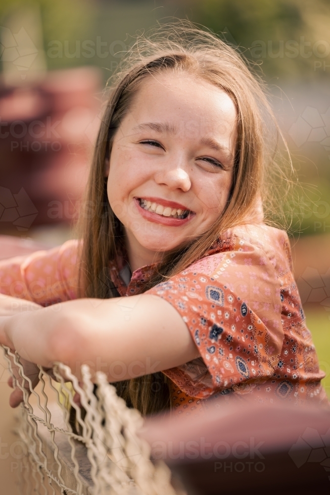 Portrait of cheerful pre-teen girl leaning on wire fence in country town - Australian Stock Image