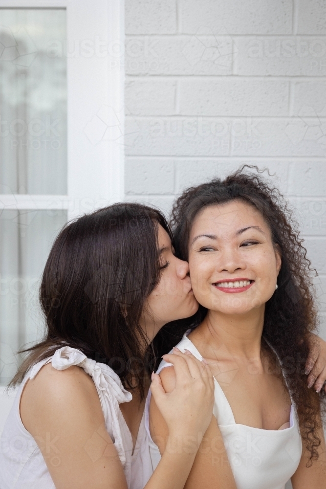 Portrait of daughter kissing mother on the cheek - Australian Stock Image