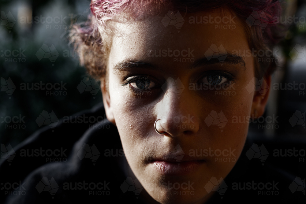 Portrait of depressed, angry teenage girl with short hair in dark, moody light - Australian Stock Image