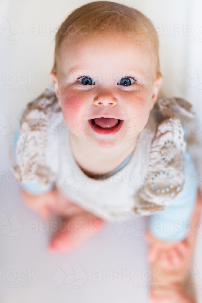 portrait of happy baby girl sitting on floor - Australian Stock Image