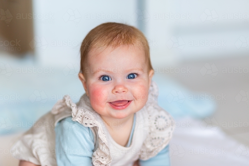 portrait of happy baby girl sitting on floor - Australian Stock Image