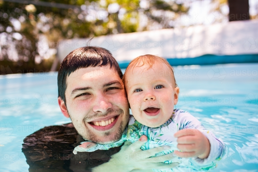 Portrait of Happy dad and baby in swimming pool together - Australian Stock Image