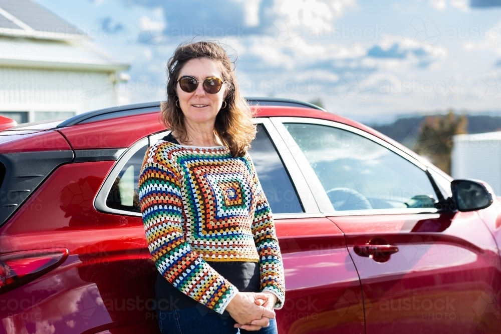 Portrait of happy middle age person standing beside electric car - Australian Stock Image