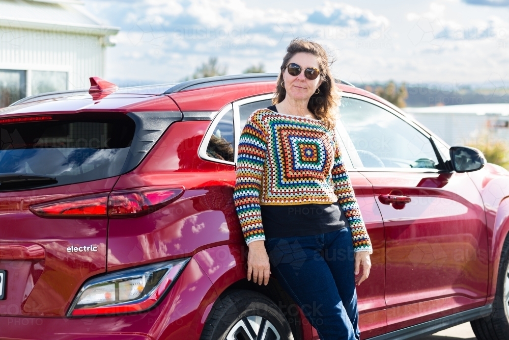 Portrait of happy middle age person standing beside ev car - Australian Stock Image