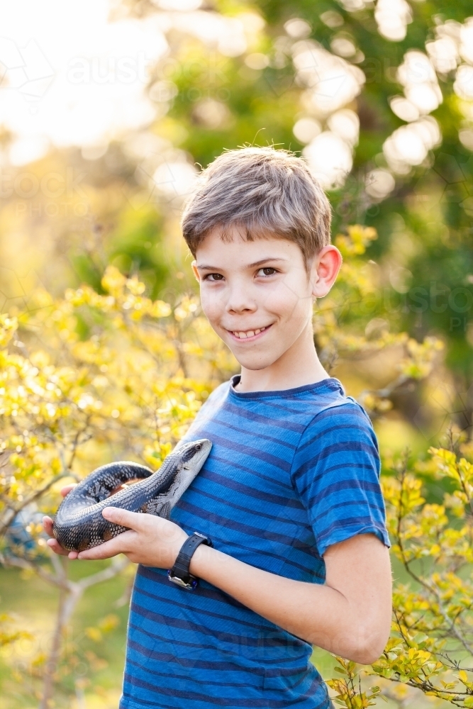 Portrait of happy tween boy with lizard outside in spring garden - Australian Stock Image