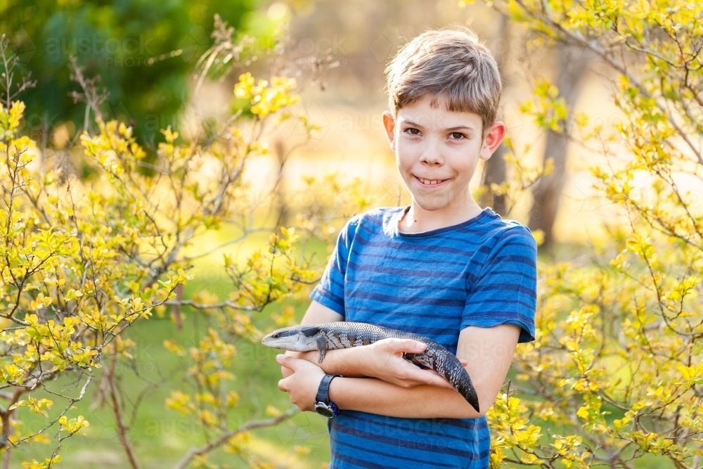 Portrait of happy tween boy with lizard outside in spring garden - Australian Stock Image