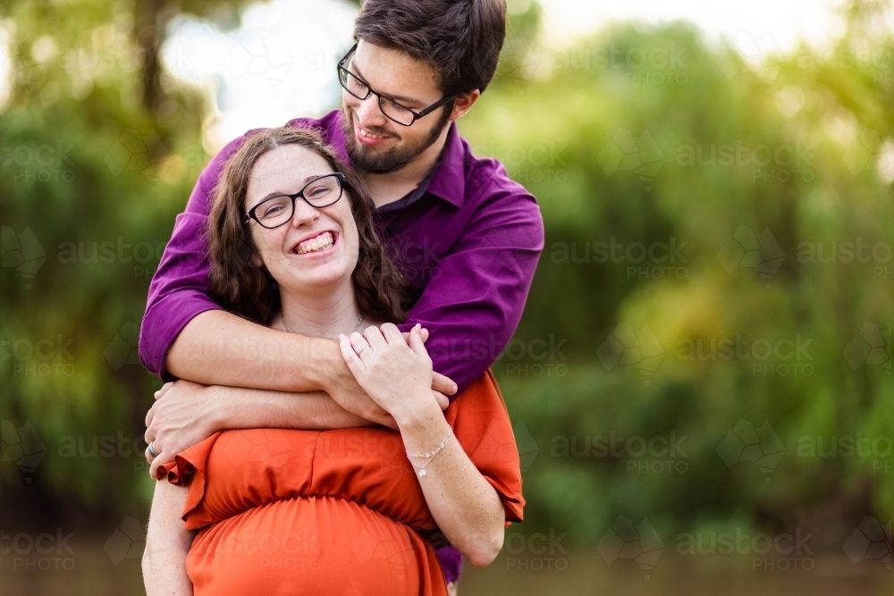 Portrait of happy young expectant parents in their twenties smiling together outside - Australian Stock Image