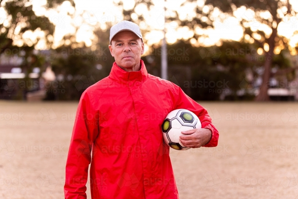 Portrait of male football coach wearing a cap and holding ball - Australian Stock Image