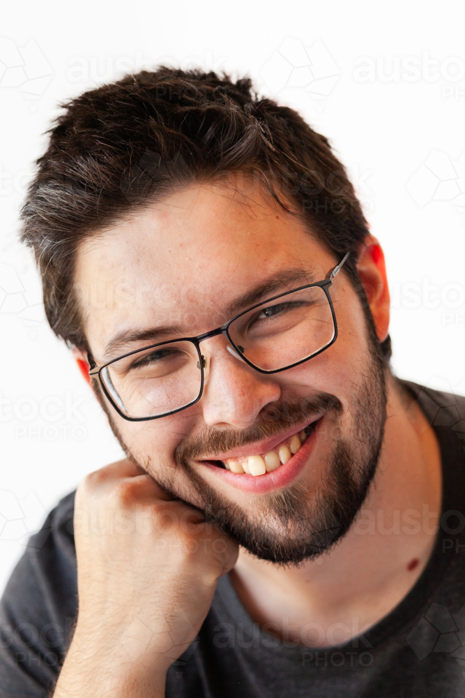 Portrait of man in his twenties resting hand on chin on white backdrop - Australian Stock Image