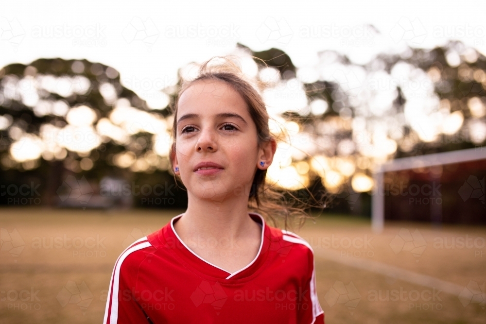 Portrait of single tween girl football player wearing a red sports uniform - Australian Stock Image