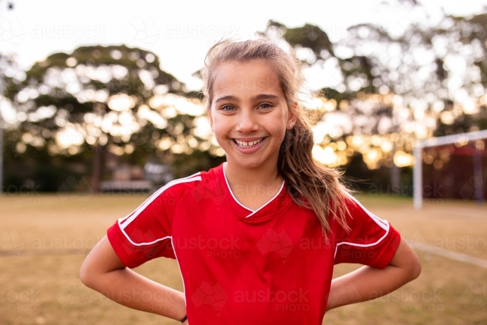 Portrait of single tween girl football player wearing a red sports uniform - Australian Stock Image