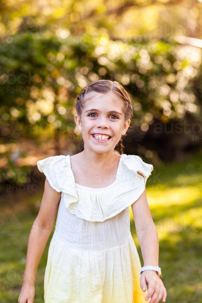 Portrait of smiling young aussie kid in yellow dress and braids outside - Australian Stock Image