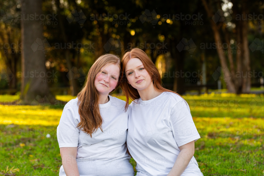 Portrait of twin seventeen year old redhead girls with heads together outdoors - Australian Stock Image