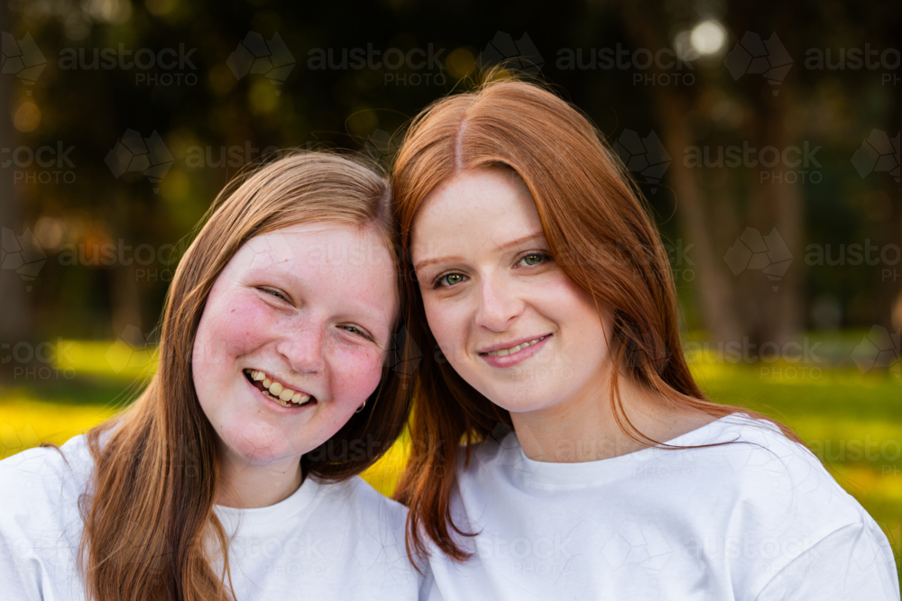 Portrait of twin seventeen year old redhead girls with heads together outdoors - Australian Stock Image