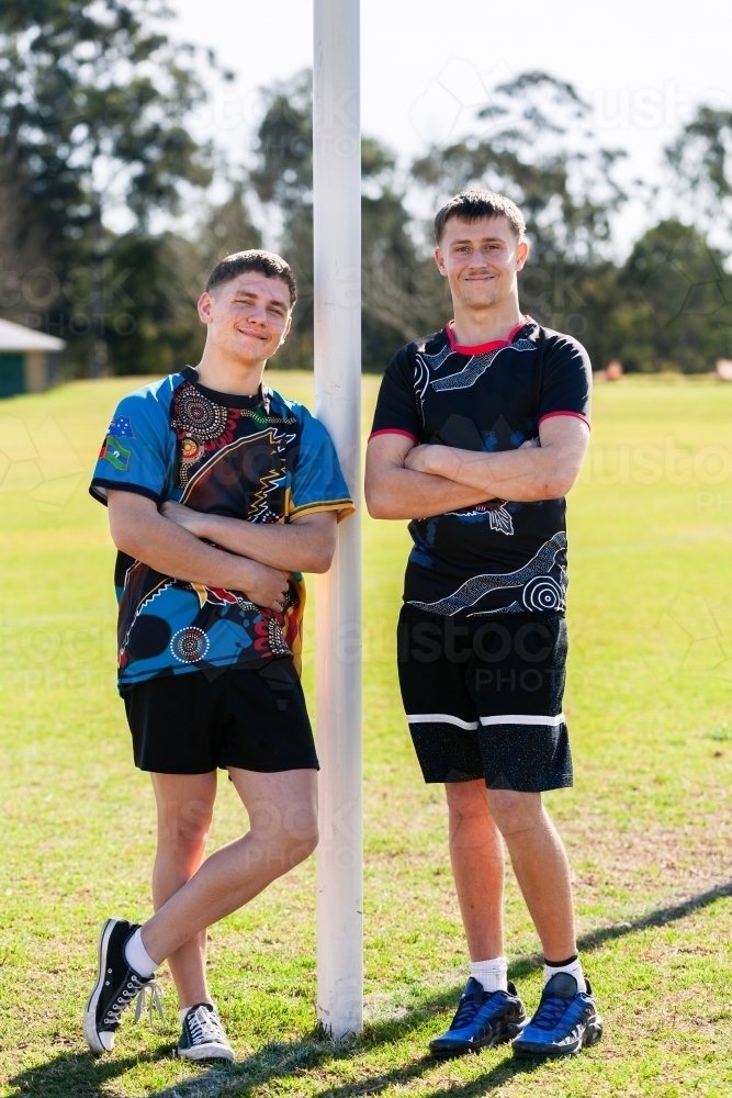 Portrait of two teen footy players leaning on goal posts - Australian Stock Image