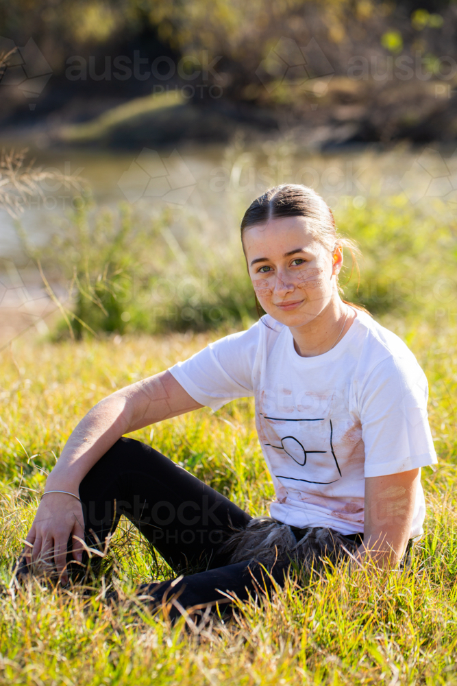 Portrait of young aboriginal person sitting in grass - Australian Stock Image