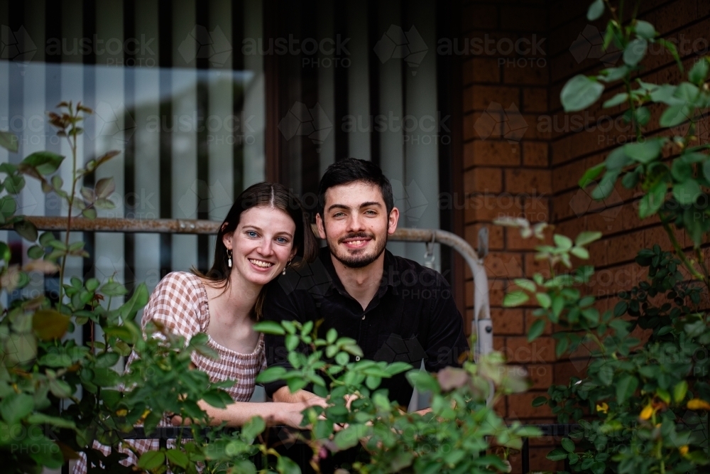 Portrait of young couple leaning on front balcony railing of home they own - Australian Stock Image